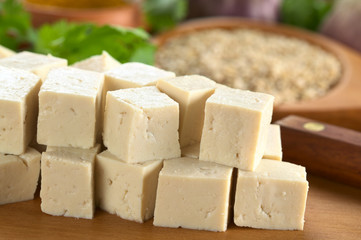 Raw tofu cut in dices on wooden board