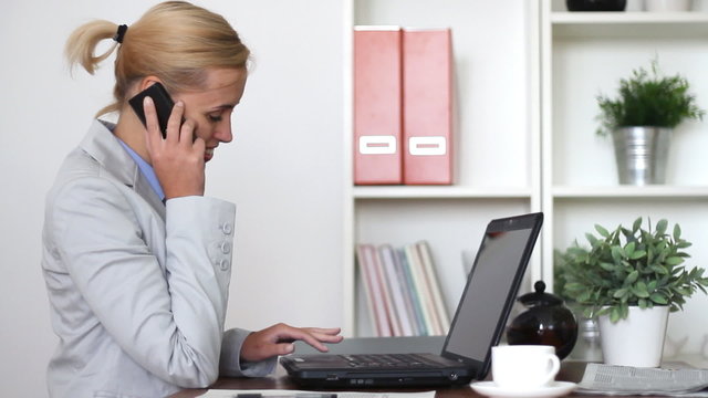 Businesswoman talking on mobile phone and working on laptop