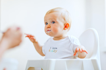 Eat smeared lovely baby in baby chair feeding by mother © Alliance