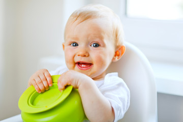 Adorable baby sitting in baby chair and playing with plate