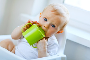 Lovely baby girl sitting in chair and drinking from baby cup © Alliance
