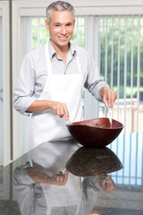 Smiling grey hair man tossing salad in apron