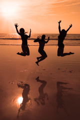 Fototapeta premium Mother and two kids silhouettes jumping on beach at sunset