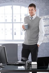 Casual businessman drinking tea in office smiling