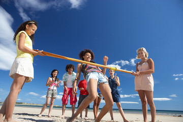 Teenagers doing limbo dance on beach - obrazy, fototapety, plakaty