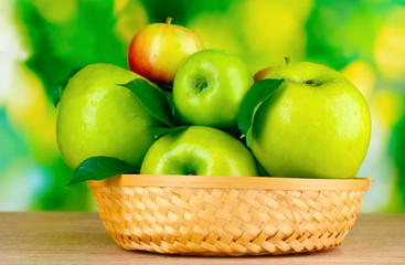 Fresh organic green apples in basket on wooden table outside