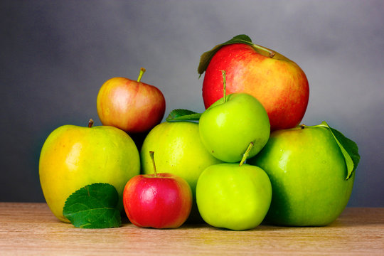Many fresh organic apples on wooden table on grey background