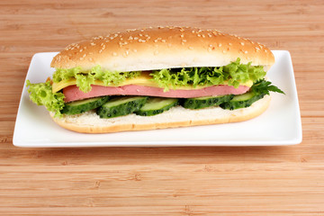 Sandwich with sausage, cheese and cucumber on plate on wooden ba