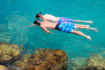 Two tourists snorkeling in clear sea water.