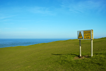 Caution Cliff Top warning sign against grassy and sea horizon