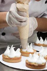 Cuisinier décorant des tartelettes de meringue avec une poche à douille