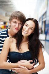 Portrait of young couple embracing at shopping mall and looking