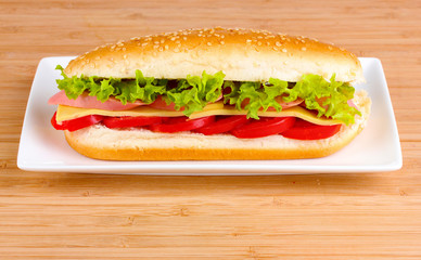 Sandwich with sausage, cheese and tomatoes on plate on wooden ba