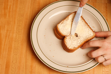 Butter being spread on a slice of white bread with a knife