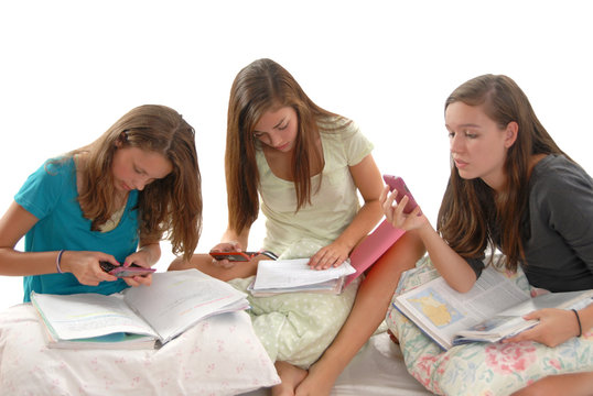 Three teenage girls doing homework books phones