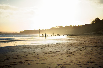 Backlit sandy beach at dusk with families walking