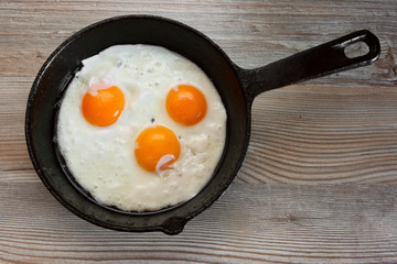 three Fried egg in frying pan on wooden table