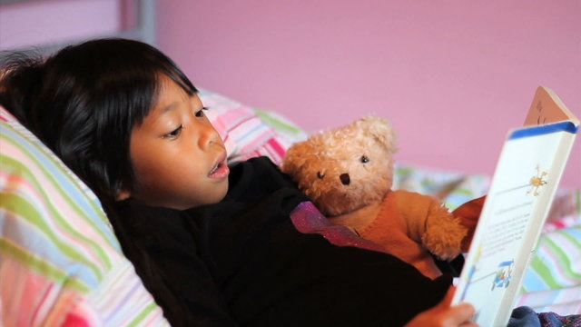 Little Asian Girl Reads Story Book To Teddy Bear
