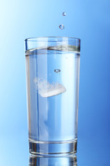 Glass with efervescent tablet in water on blue background