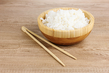 Wooden bowl of cooked rice and chopsticks on wooden table
