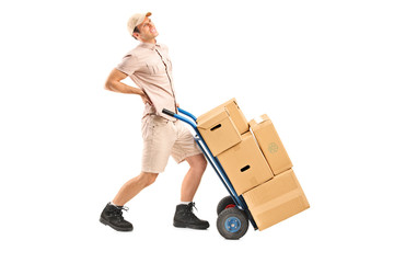 Delivery boy, suffering from a back pain, pushing a hand truck