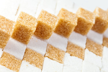Cubes of not refined reed sugar lie on pieces of white sugar..