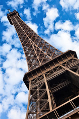 Eiffel tower tilted view over blue sky with white clouds.