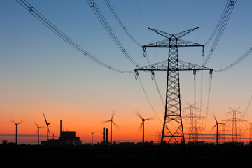 Strommast bei Sonnenuntergang mit Windrädern und Kernkraftwerk