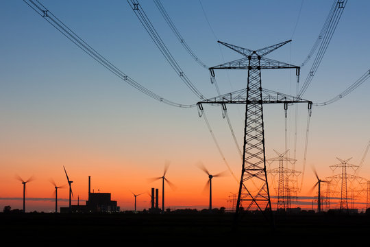 Strommast bei Sonnenuntergang mit Windr&auml;dern und Kernkraftwerk