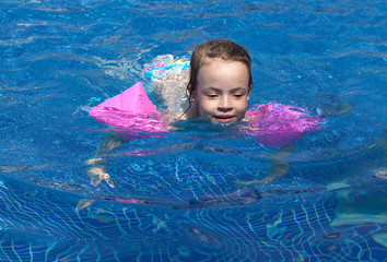 Joyful little girl swimming in the pool.
