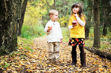 Little boy and little girl eating apples in forest