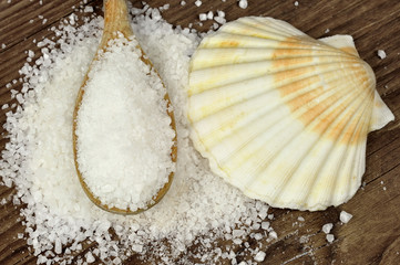 Coarse sea salt on a wooden table with spoon and scallop shell