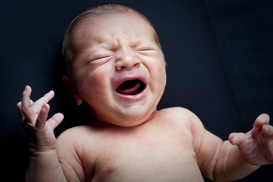 portrait of adorable newborn baby girl crying on black backgroun