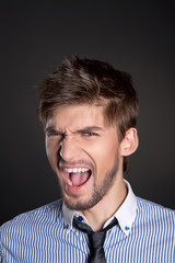 Young business man emotional scream over gray background