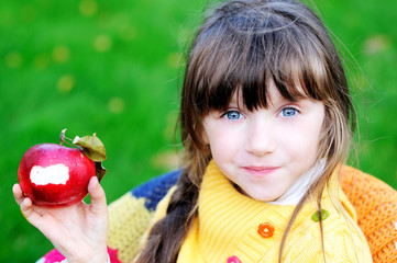 Funny child girl eating apple outdoors
