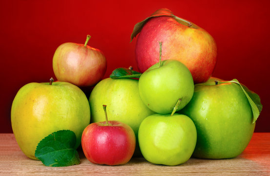 Many fresh organic apples on wooden table on red background