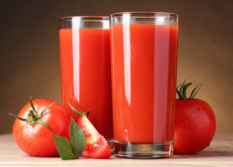Tomato juice in glasses and tomato on wooden table on brown back