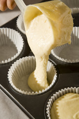 Vanilla cake-mix being poured into cupcake forms