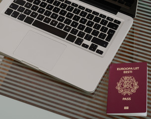 Laptop, passport  placed on a glass tabletop.