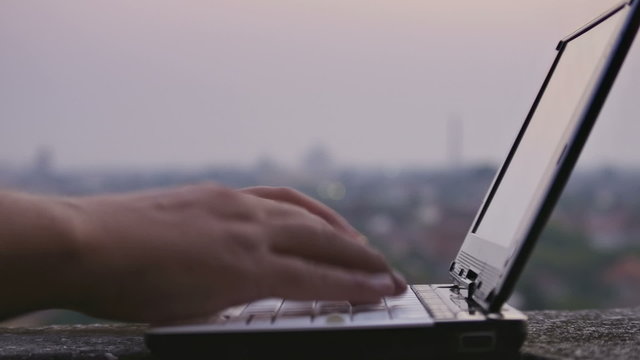 typing on netbook with out of focus city at sunset