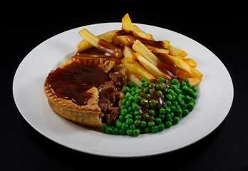 Close up of Steak Pie and chips with peas and gravy.