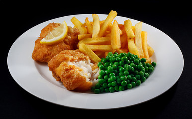 Close up of fish and chips with peas and a slice of lemon.