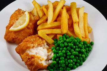 Close up of fish and chips with peas and a slice of lemon.