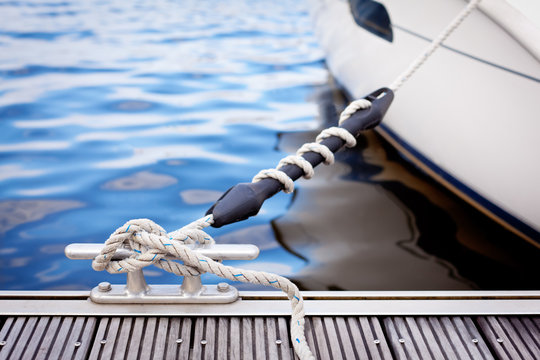 Fototapeta A white yacht moored with a line tied around a metal fixing