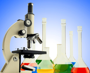 Laboratory metal microscope and test tubes with liquid over blue