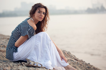brunette woman sitting on stone beach