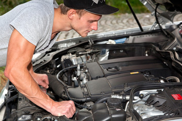 Junger Mann blickt unter die Motorhaube vom PKW