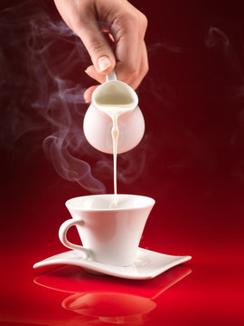 hand pouring milk in coffee cup