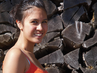 smiling girl in front of a stack of wood