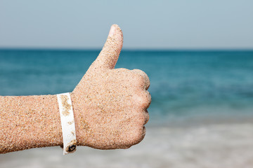 Hand gesturing thumb up on sea beach